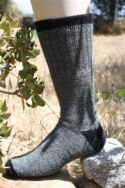 Gray OutdoorAdventure alpaca sock with black trim worn standing on rocks in dry grass