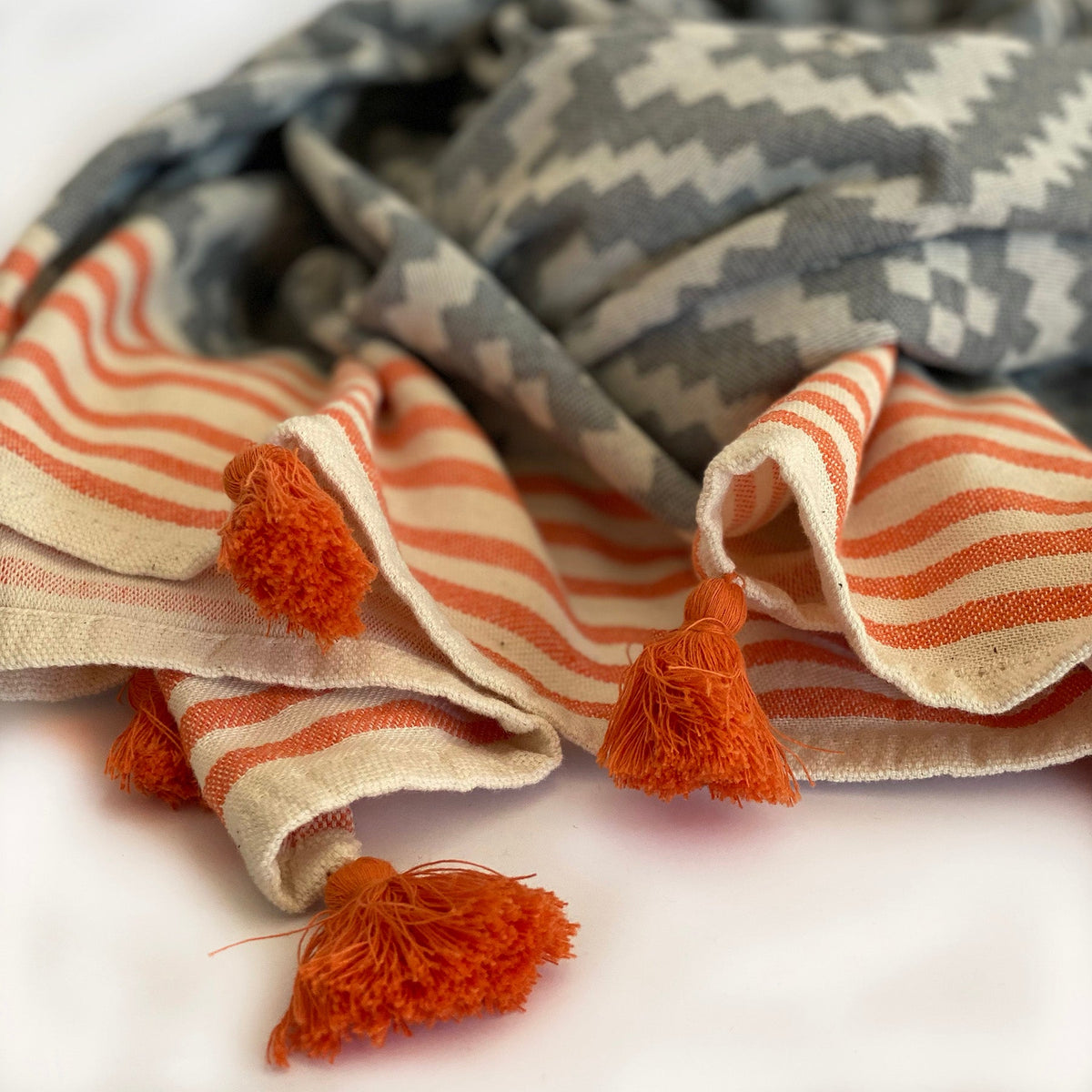 Closeup of the orange striped edge and tassels on the gray Hilana Merida Turkish towel