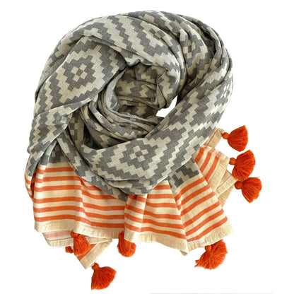 Gray and cream Hilana Merida Turkish beach towel rolled up showing its orange-striped ends and tassels