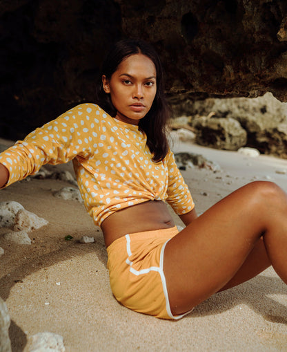 Model seated on the sand wearing GIRL Seaside Runner recycled shorts in sunflower yellow