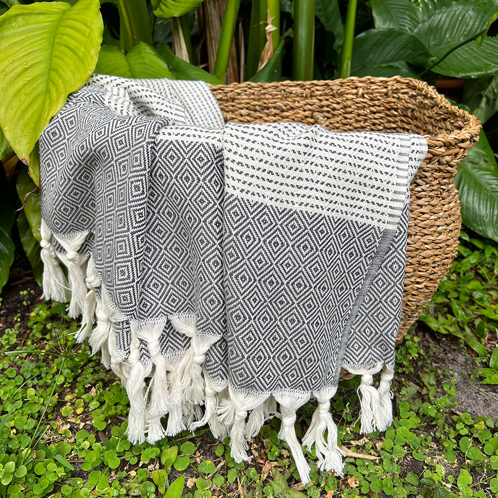 Black and cream diamond stripe Turkish throw draped over a woven basket among tropical plants