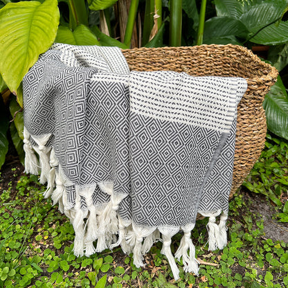 Black and cream diamond stripe Turkish throw draped over a woven basket among tropical plants