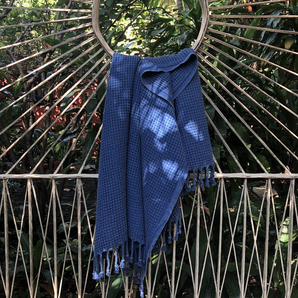 Blue waffle weave Turkish towel draped over a rattan peacock chair outdoors