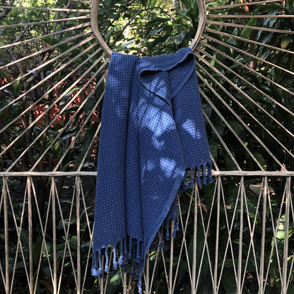 Blue waffle weave Turkish towel draped over a rattan peacock chair outdoors