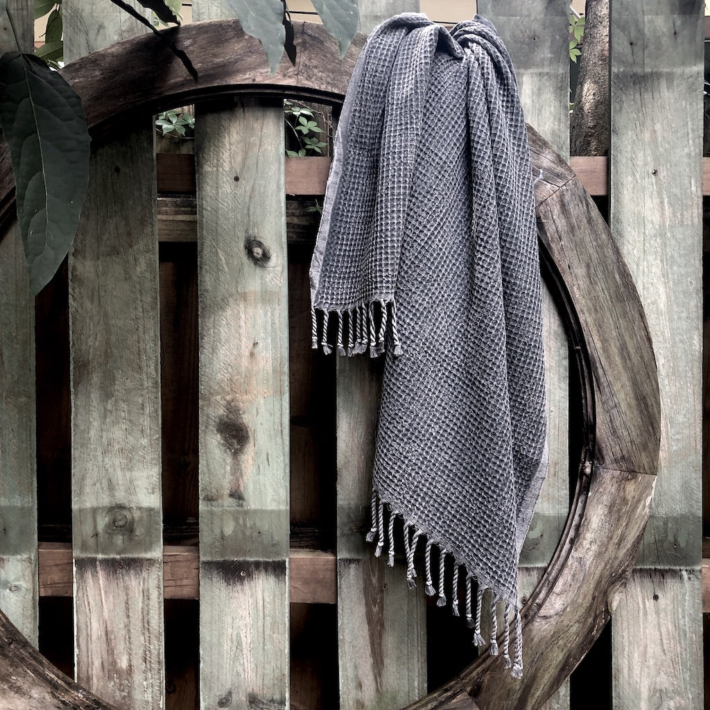 Charcoal gray waffle weave Turkish towel draped over a rustic wooden fence