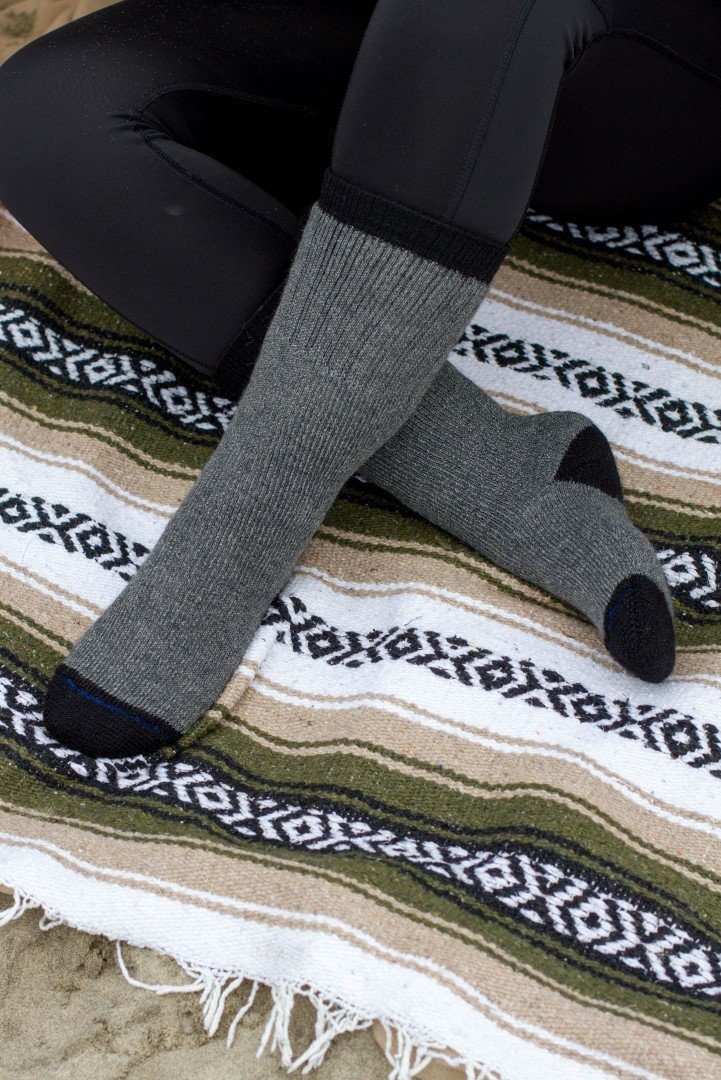 Person wearing gray OutdoorAdventure alpaca socks with black heels and toes, sitting on a patterned blanket