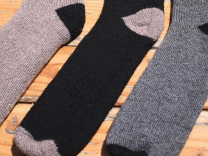 Three OutdoorAdventure alpaca socks in gray, black, and dark gray lying flat on wood