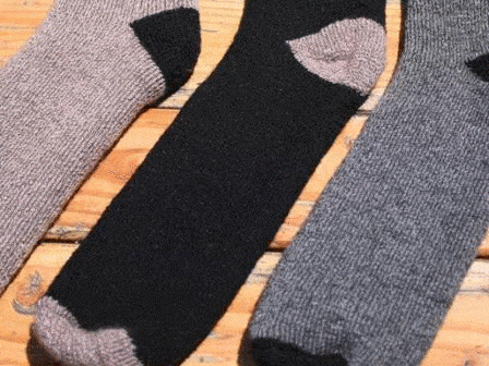Three OutdoorAdventure alpaca socks in gray, black, and dark gray lying flat on wood