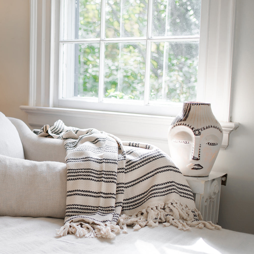 White Turkish throw with fine black stripes and tassel fringe draped over a cream sofa
