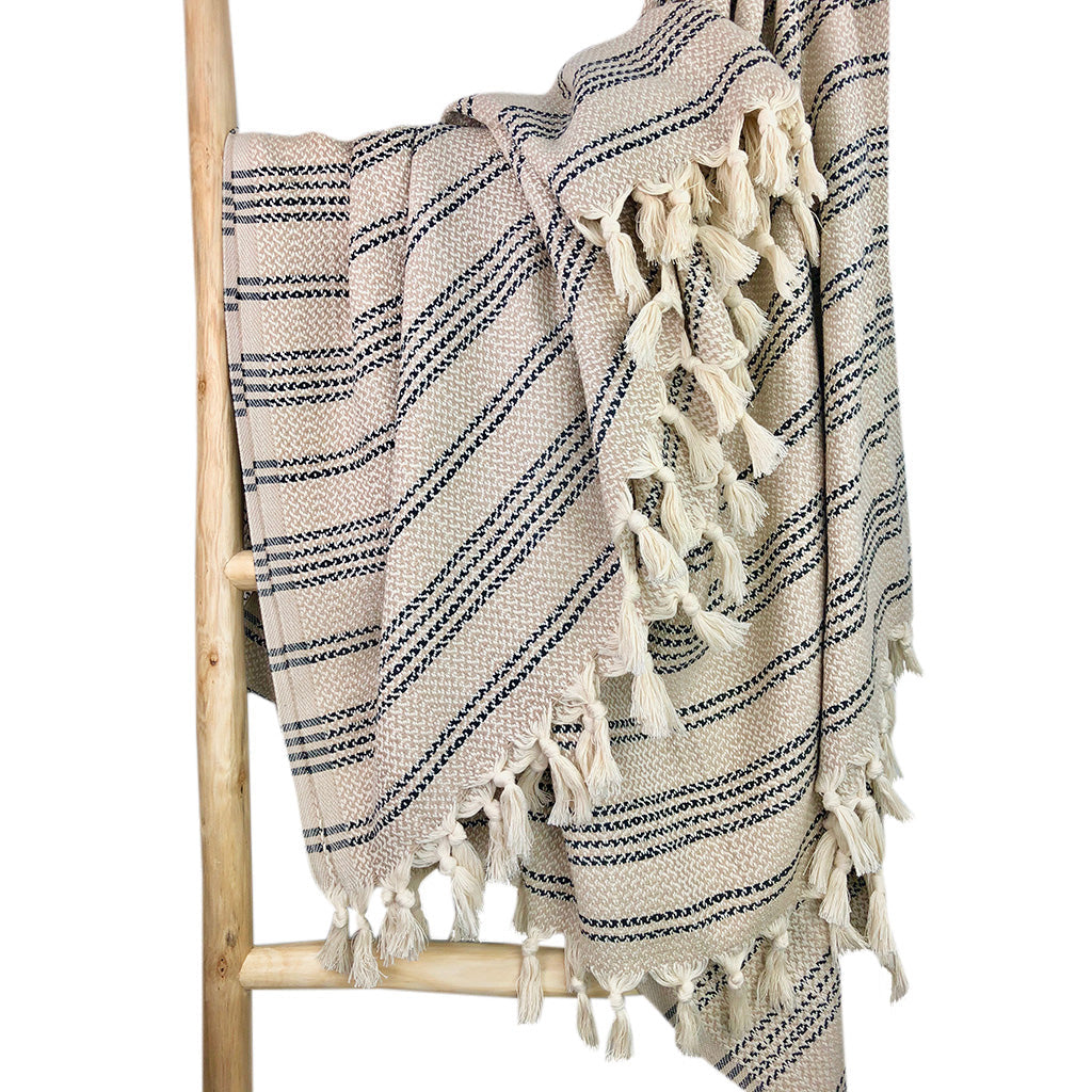 Beige and taupe striped Turkish throw with rows of cream tassels on a wooden ladder