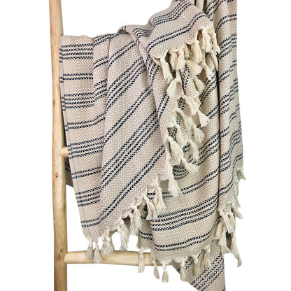 Beige and taupe striped Turkish throw with rows of cream tassels on a wooden ladder