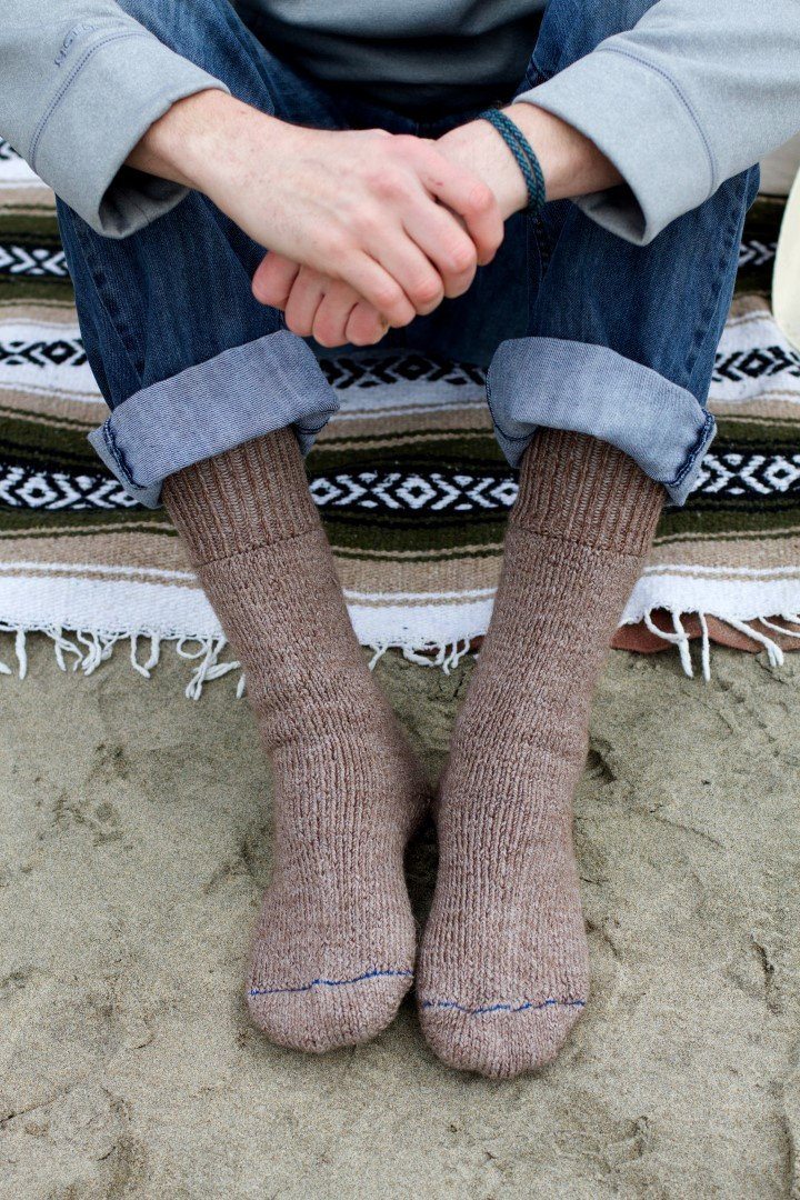 Person sitting on a woven blanket wearing brown Superwarm alpaca socks with cuffed jeans