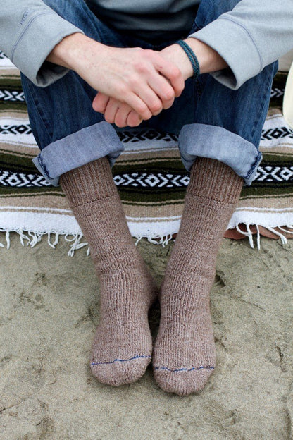 Person sitting on a woven blanket wearing brown Superwarm alpaca socks with cuffed jeans