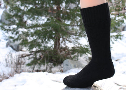 Black knee-high Superwarm alpaca sock worn standing on a rock in the snow