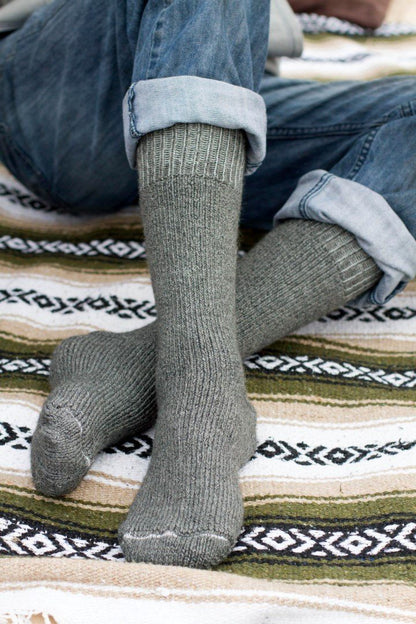 Gray Superwarm alpaca socks worn with cuffed jeans while sitting on a patterned blanket