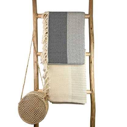 Black and gray diamond stripe Turkish throws draped over a wooden blanket ladder beside a round woven bag
