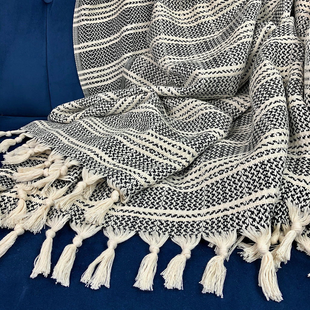 Black and cream striped Turkish throw with knotted tassels spread over a navy velvet chair
