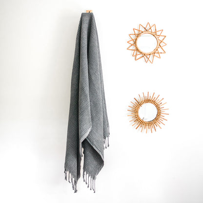 Gray waffle weave Turkish towel hanging on a wall hook beside rattan sunburst mirrors