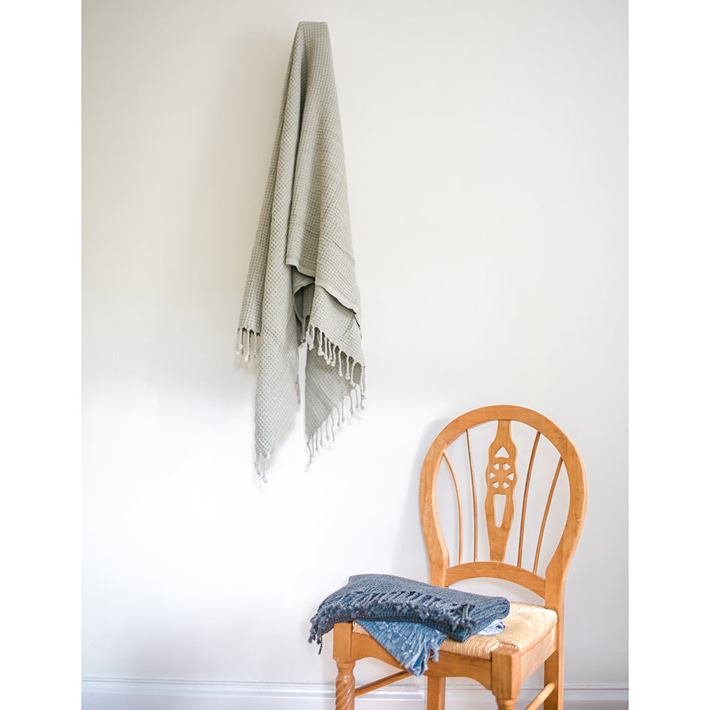 Light gray waffle weave Turkish towel on a wall hook with folded blue and charcoal towels on a chair